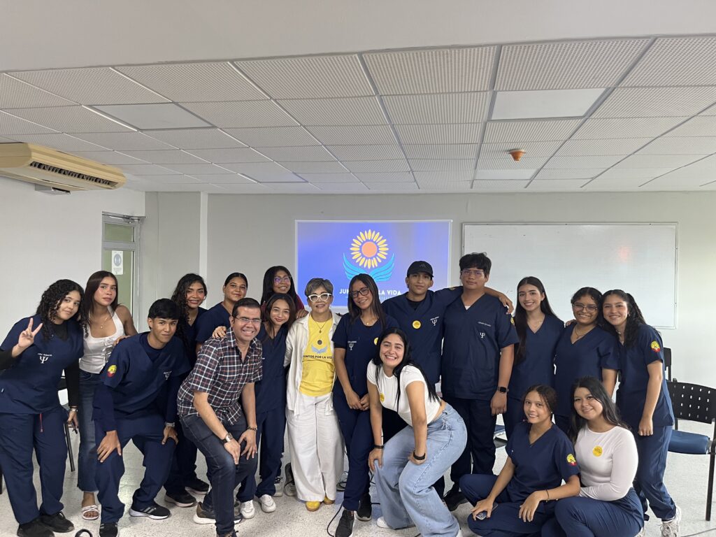 Estudiantes con uniforme azul posan junto a la Dra. Maribel Orozco al final de la charla-taller, frente a la pantalla con el logo de la fundación.