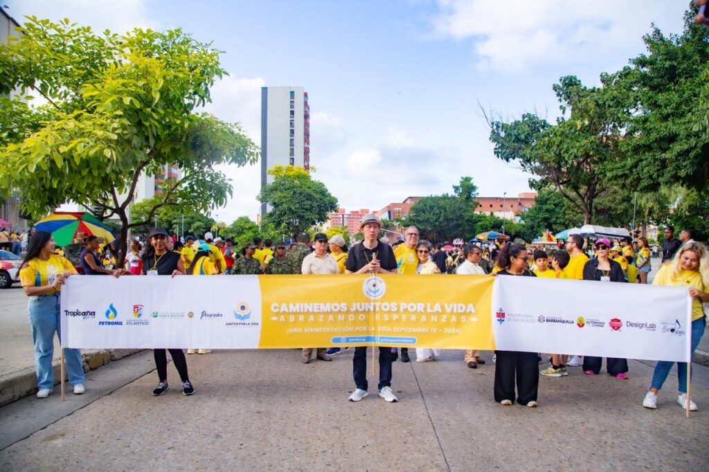 Un grupo sostiene la pancarta de «Caminemos Juntos por la Vida» en plena calle, rodeado de asistentes vestidos de amarillo.