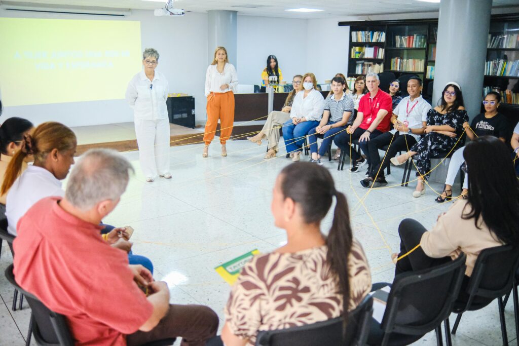 Los participantes, sentados en círculo, sostienen una cuerda amarilla que forma una red entre todos durante la jornada.