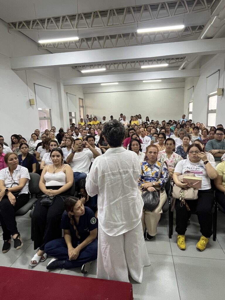 Un auditorio lleno escucha a la Dra. Maribel Orozco, de espaldas a la cámara, durante el encuentro con la Arquidiócesis.