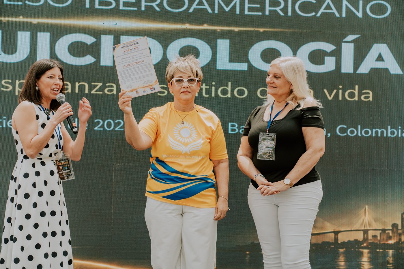 Maribel Orozco mostrando un reconocimiento junto a dos asistentes en la tarima.